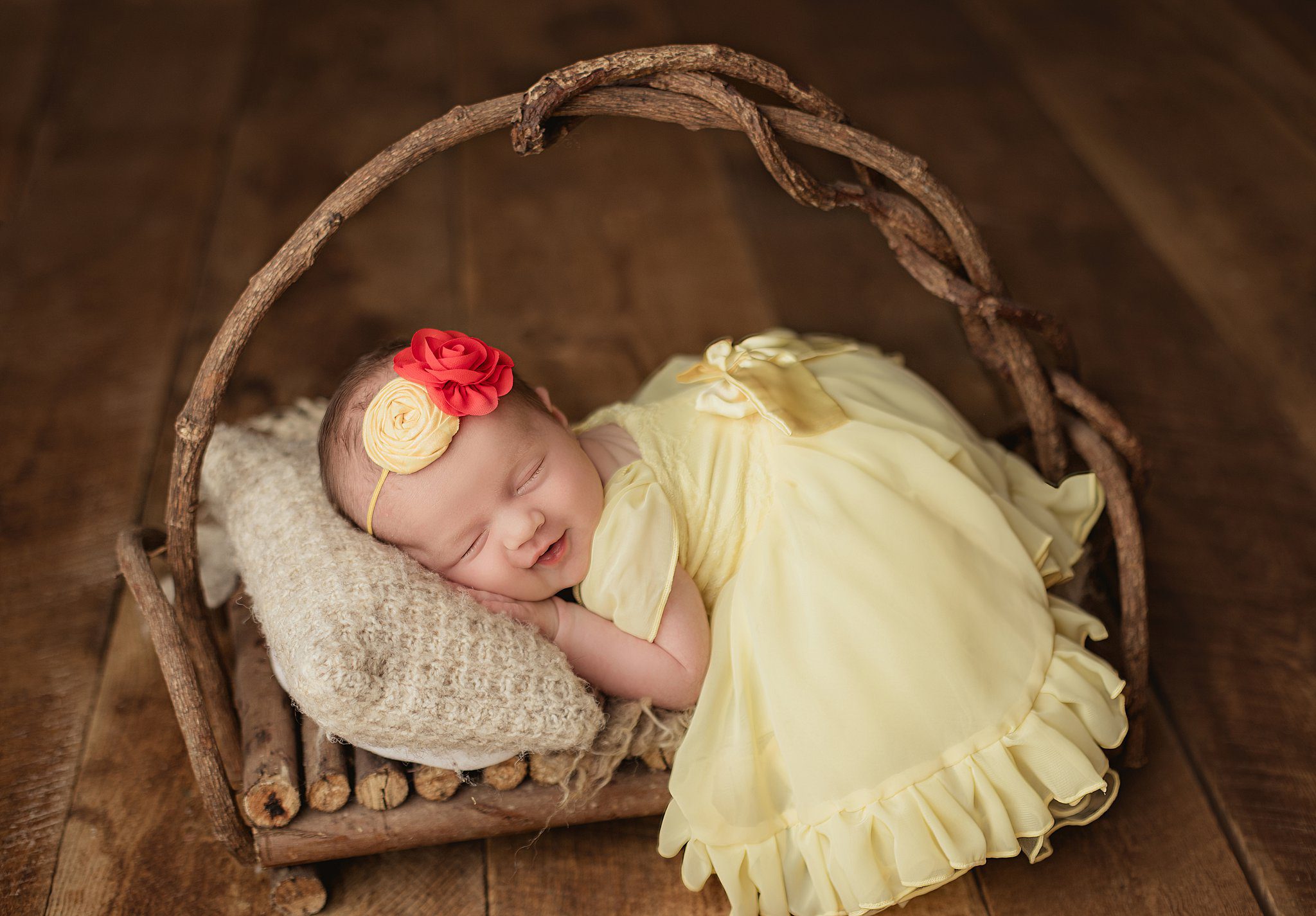 A newborn baby girl sleeps on a rustic wooden bed in a yellow dress and floral headband thanks to orange county birth center