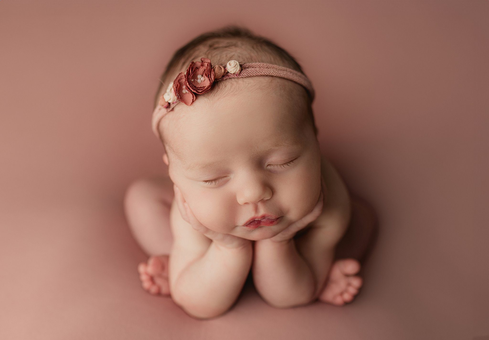 A newborn baby sleeps in a light red floral headband while resting her head in her hands thanks to orange county birth center