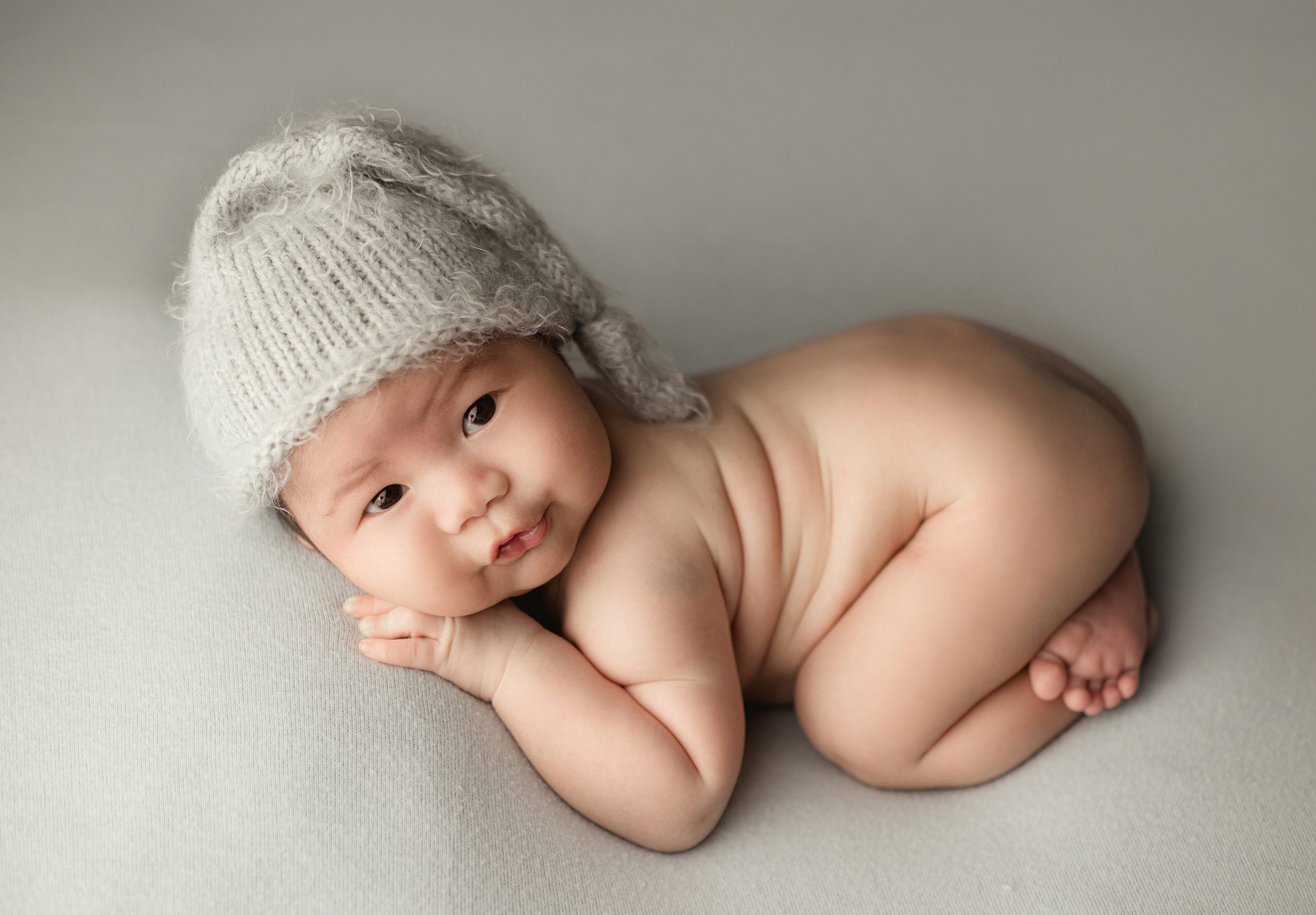 A newborn baby lays on a pad in only a knit night cap in froggy pose after meeting orange county doulas