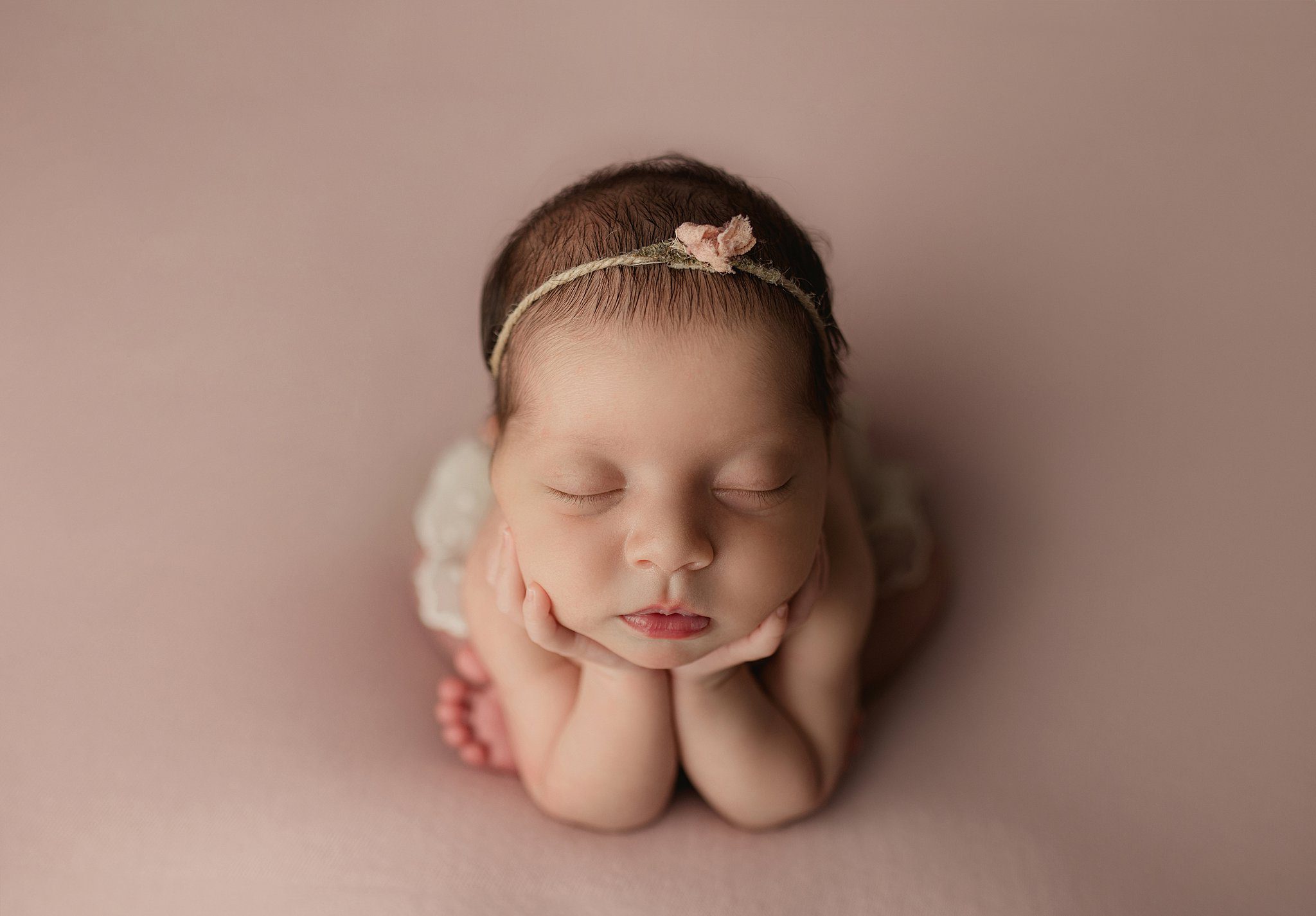 A newborn baby girl sleeps while resting her head on her hands in a studio before some things to do in anaheim with kids