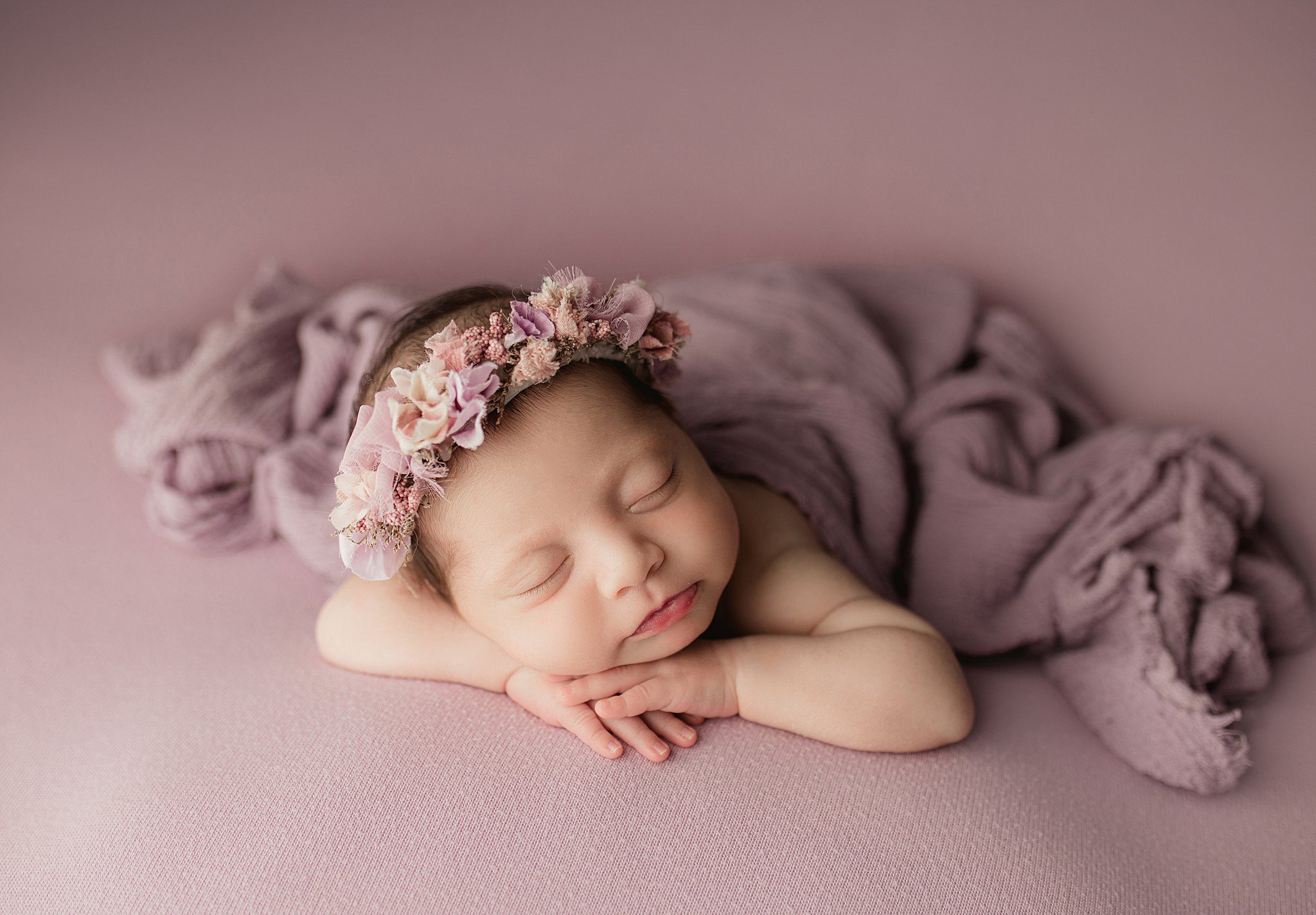 A newborn baby sleeps on a purple bed on her hands in a floral headband before some things to do in anaheim with kids