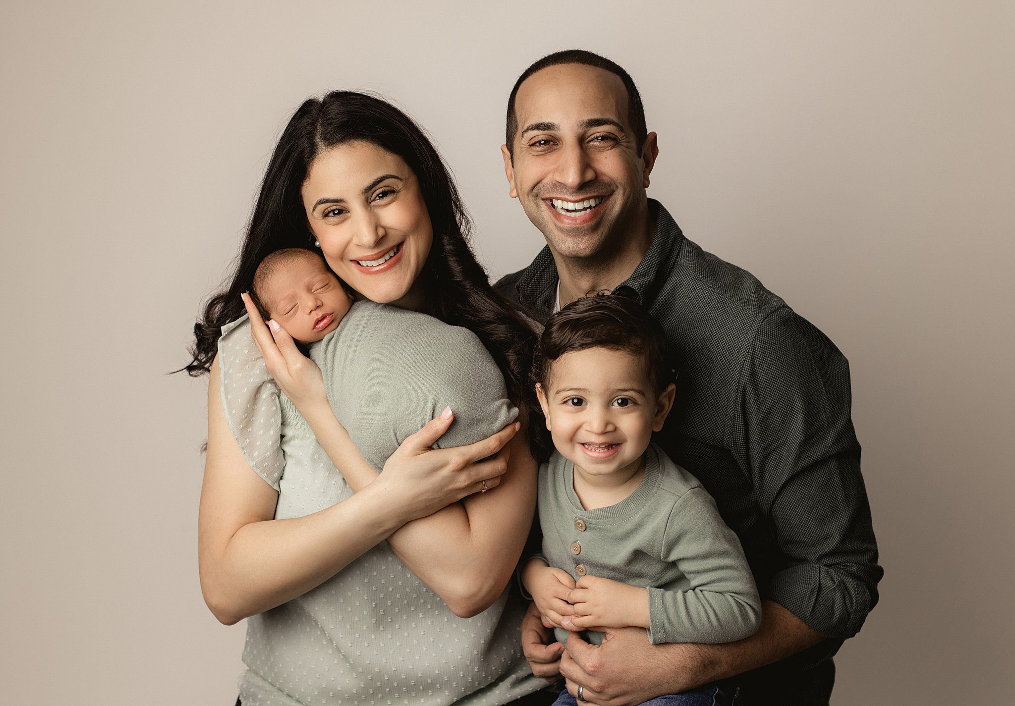 A mother and father laugh with their toddler son as mom cradles their sleeping newborn baby before some things to do in orange county with kids