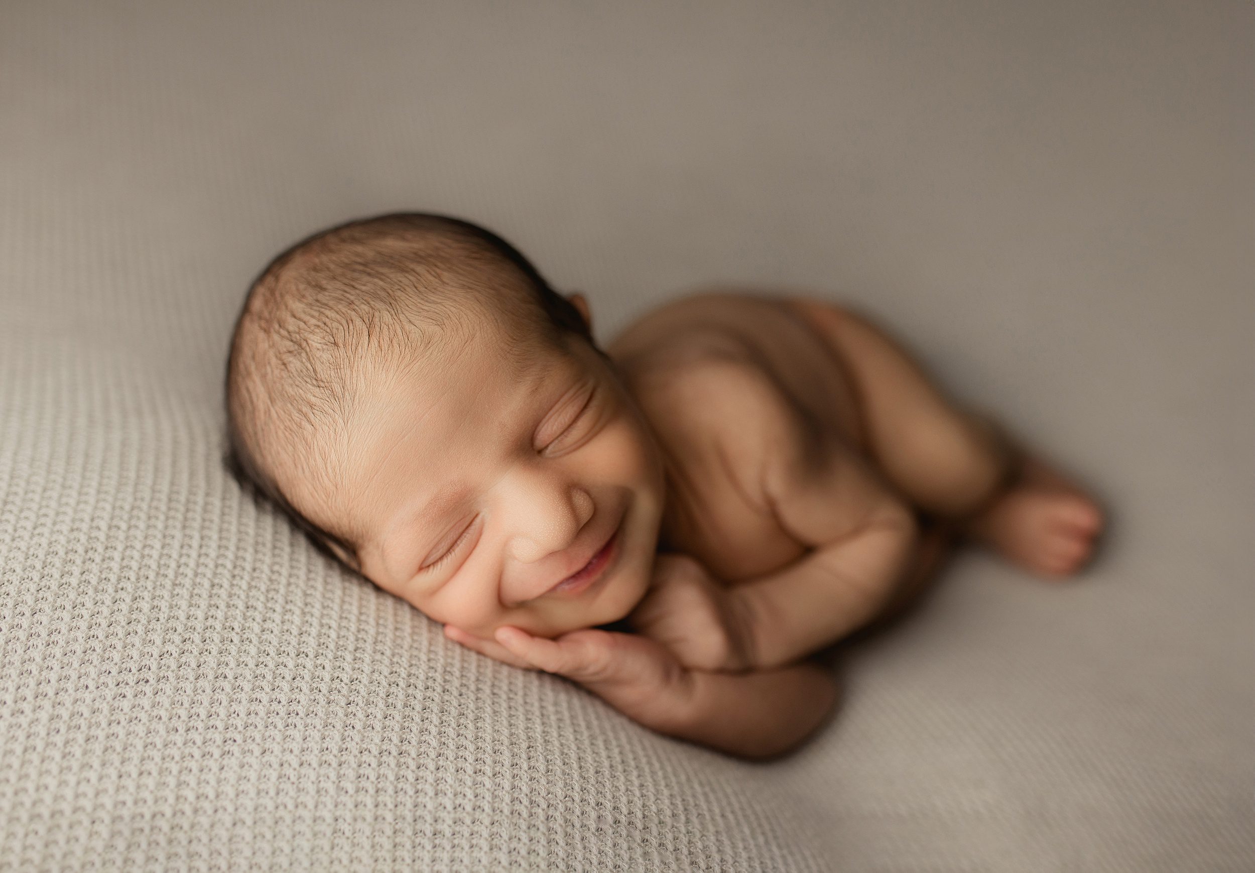 A newborn baby sleeps on its side while smiling in a studio