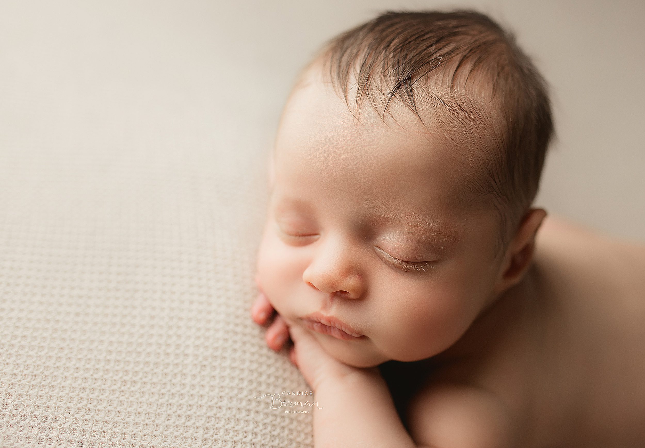 A newborn baby sleeps on its belly on a bed in a studio thanks to fertility acupuncture orange county