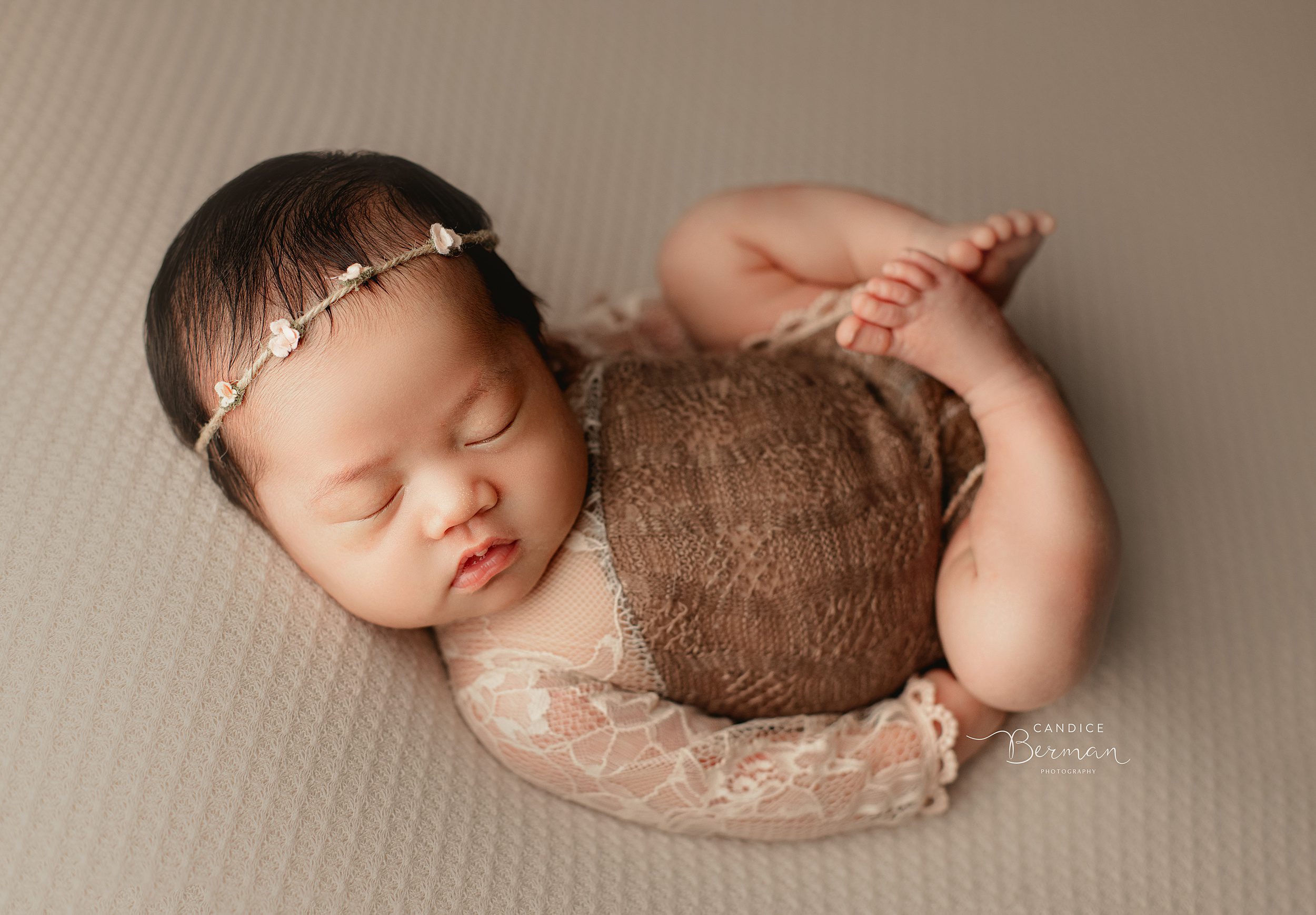 A newborn baby sleeps in a bed in a lace onesie in a studio