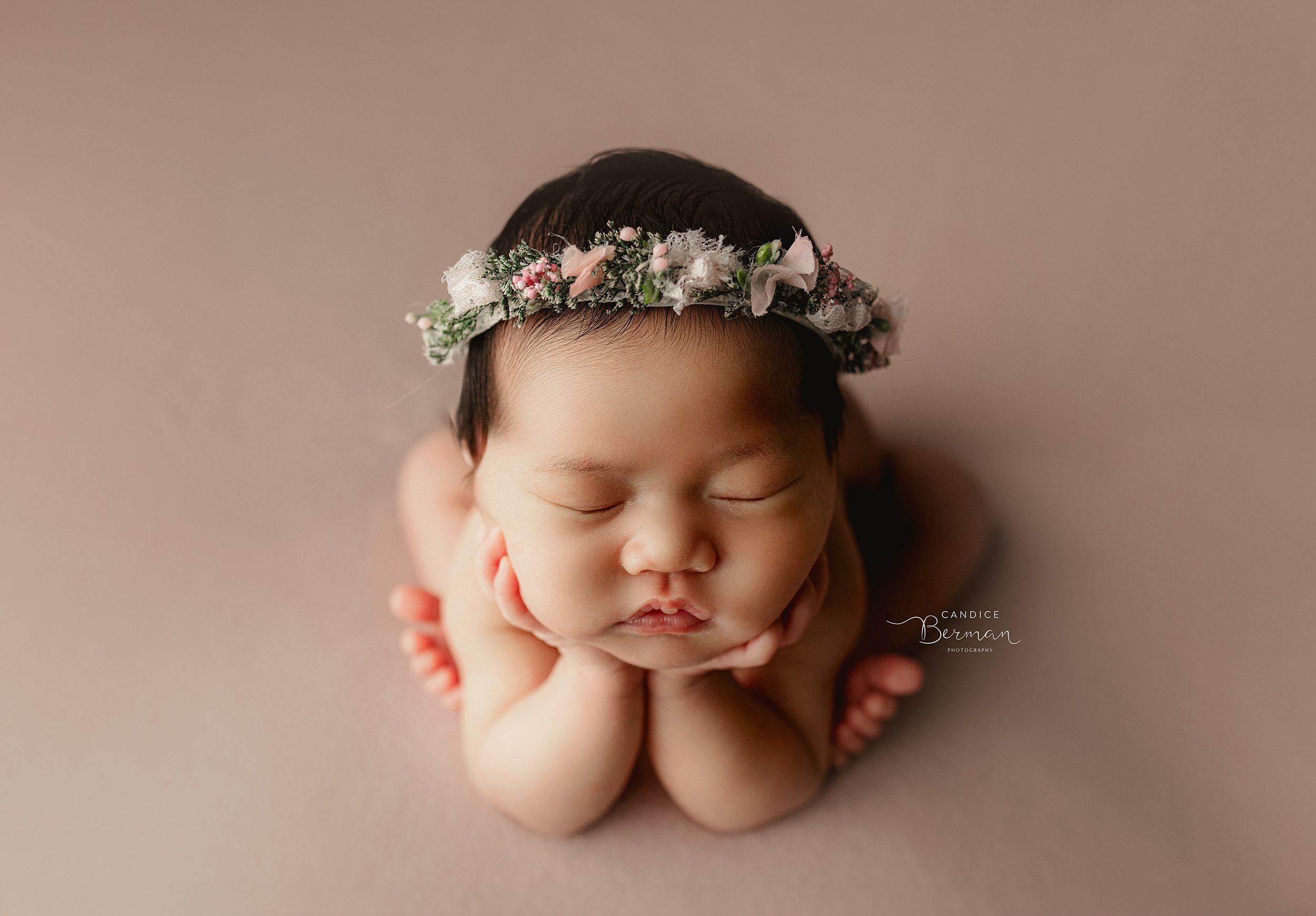 A newborn baby rests her head on her hands while sleeping in a floral headband after mom used orange county baby shower venues