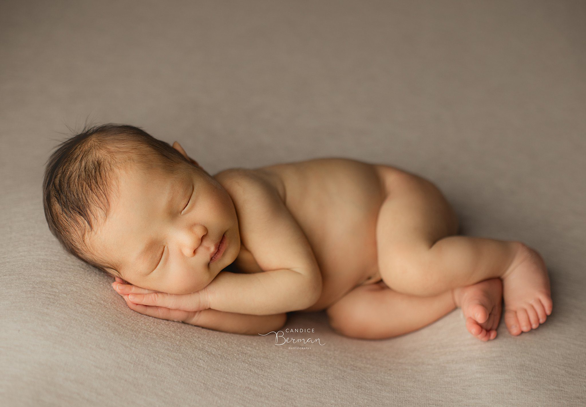 A newborn baby sleeps on its side resting its head on its hands in a studio